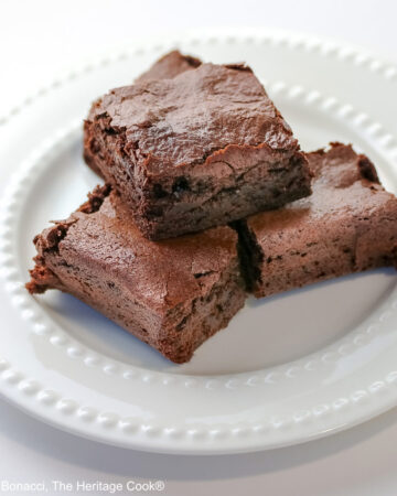 The Best Chewy Brownies, rich and so chocolatey, stacked on a white plate with two rows of white pearls, sitting on a white background; some shots of the cookbook, “Bittersweet” by Alice Medrich; © 2025 Jane Bonacci, The Heritage Cook.