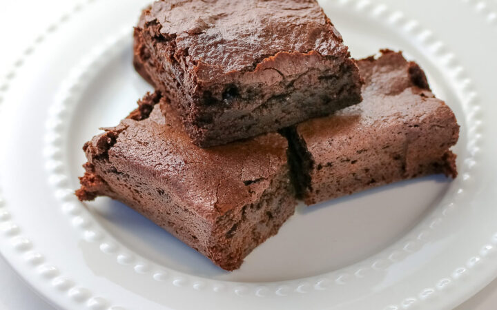 The Best Chewy Brownies, rich and so chocolatey, stacked on a white plate with two rows of white pearls, sitting on a white background; some shots of the cookbook, “Bittersweet” by Alice Medrich; © 2025 Jane Bonacci, The Heritage Cook.