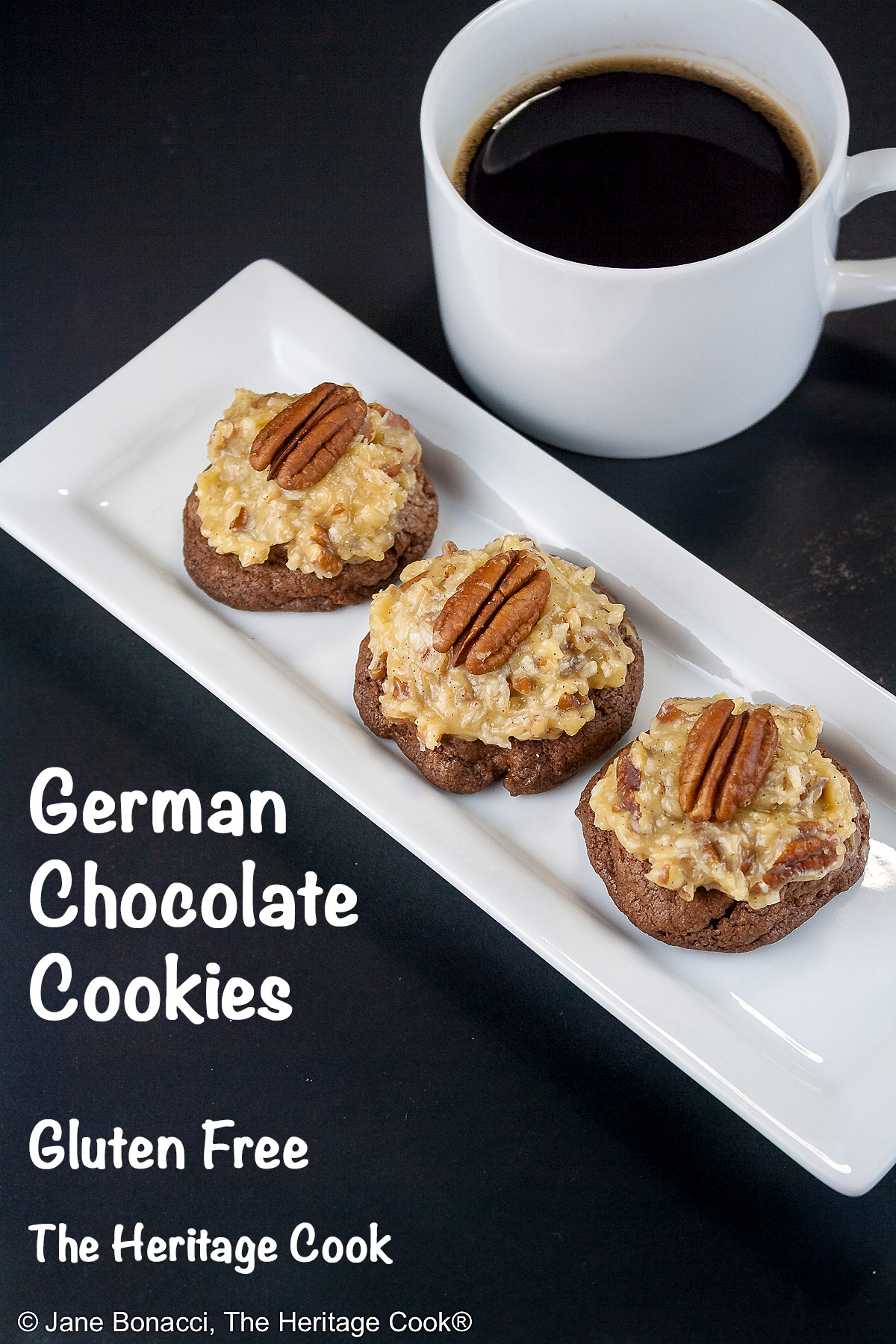 Three German Chocolate Cookies, chocolate cookies with coconut-pecan frosting on top, on a white rectangular platter with a cup of coffee behind on a black background © 2025 Jane Bonacci, The Heritage Cook.