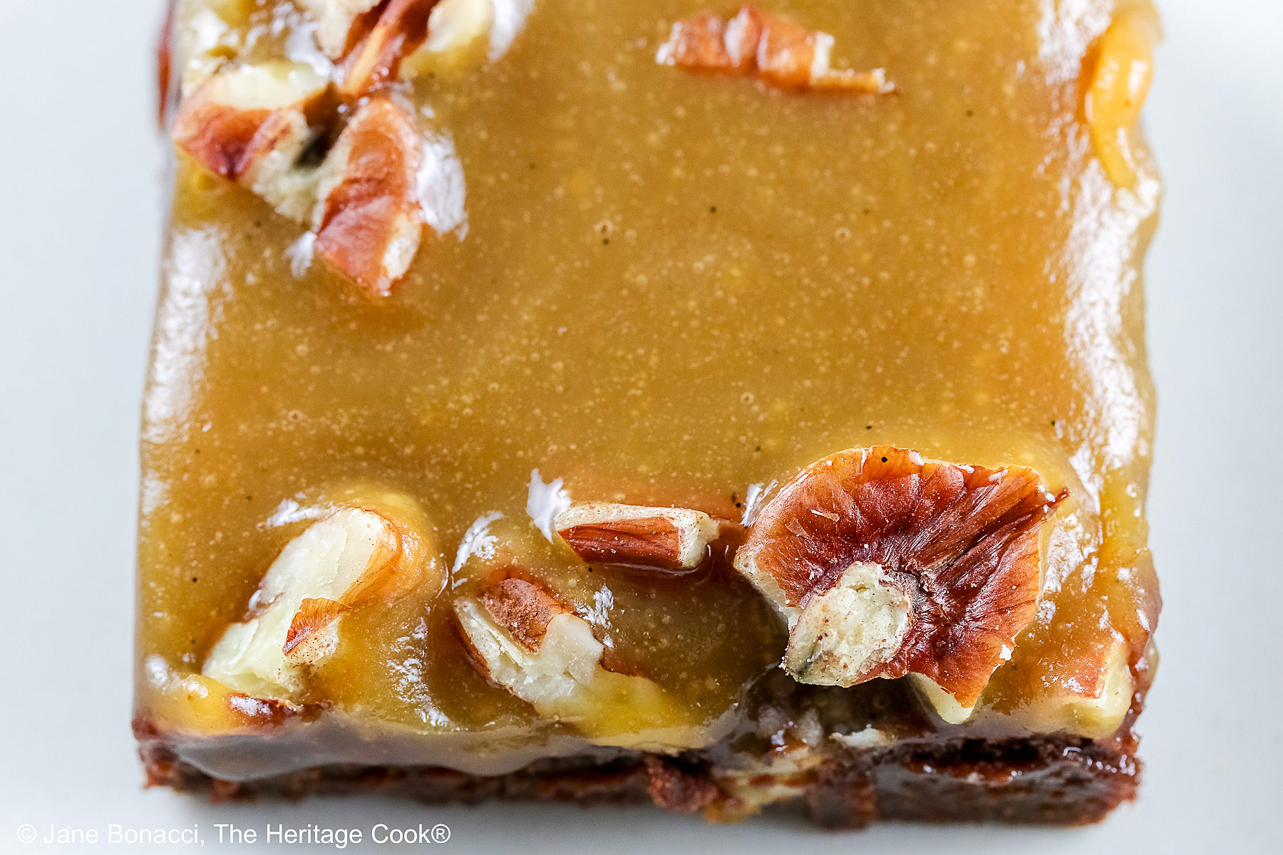 Line of 3 caramel coated brownies on a long rectangular white platter, sitting on a black background, close up of the brownies © 2026 Jane Bonacci, The Heritage Cook.