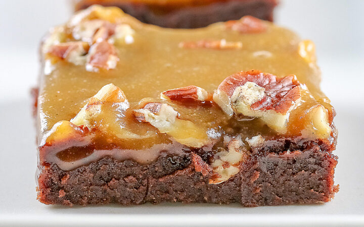Line of 3 caramel coated brownies on a long rectangular white platter, sitting on a black background, close up of the brownies © 2026 Jane Bonacci, The Heritage Cook.