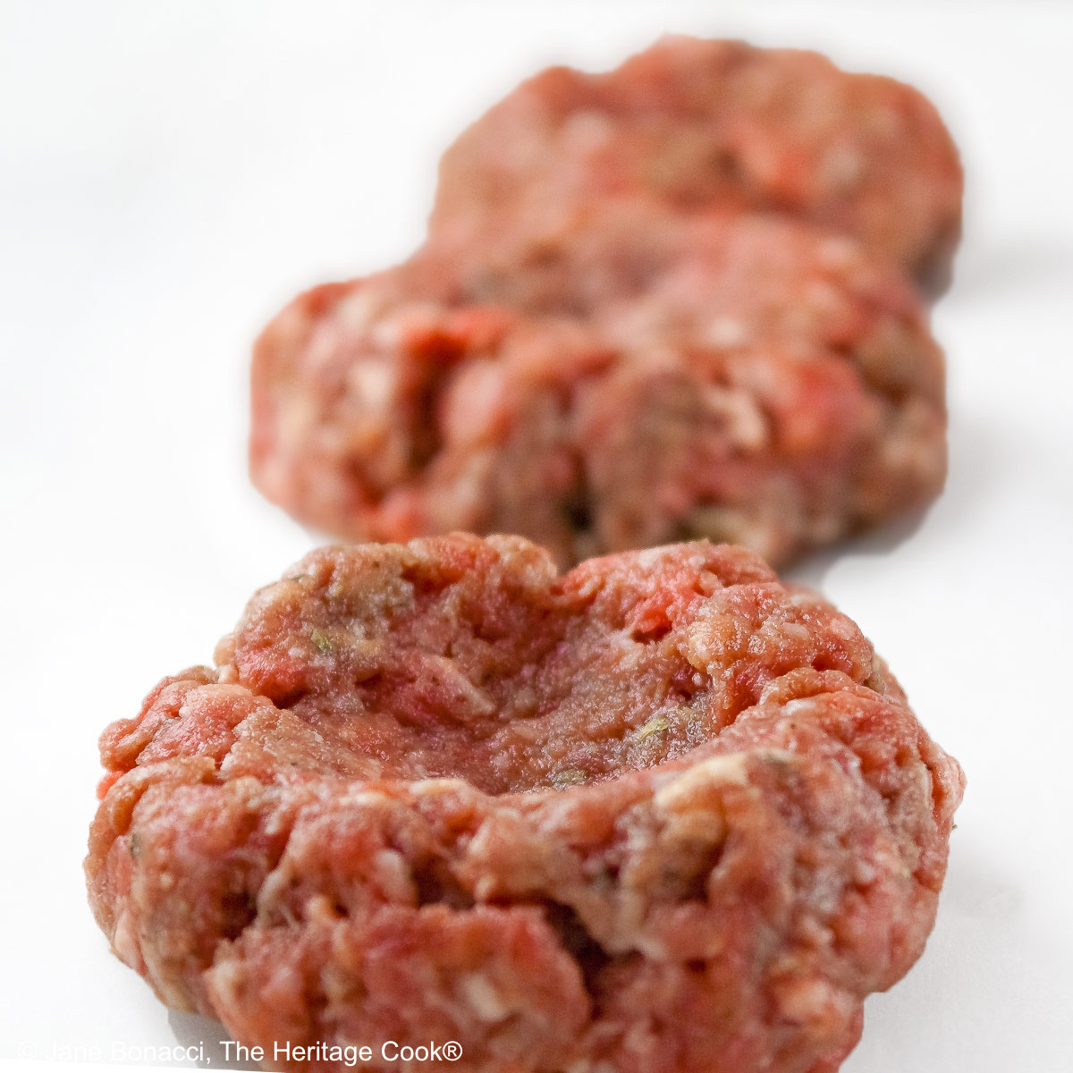 Line of 3 raw slider meatballs with an indentation pressed into each one.