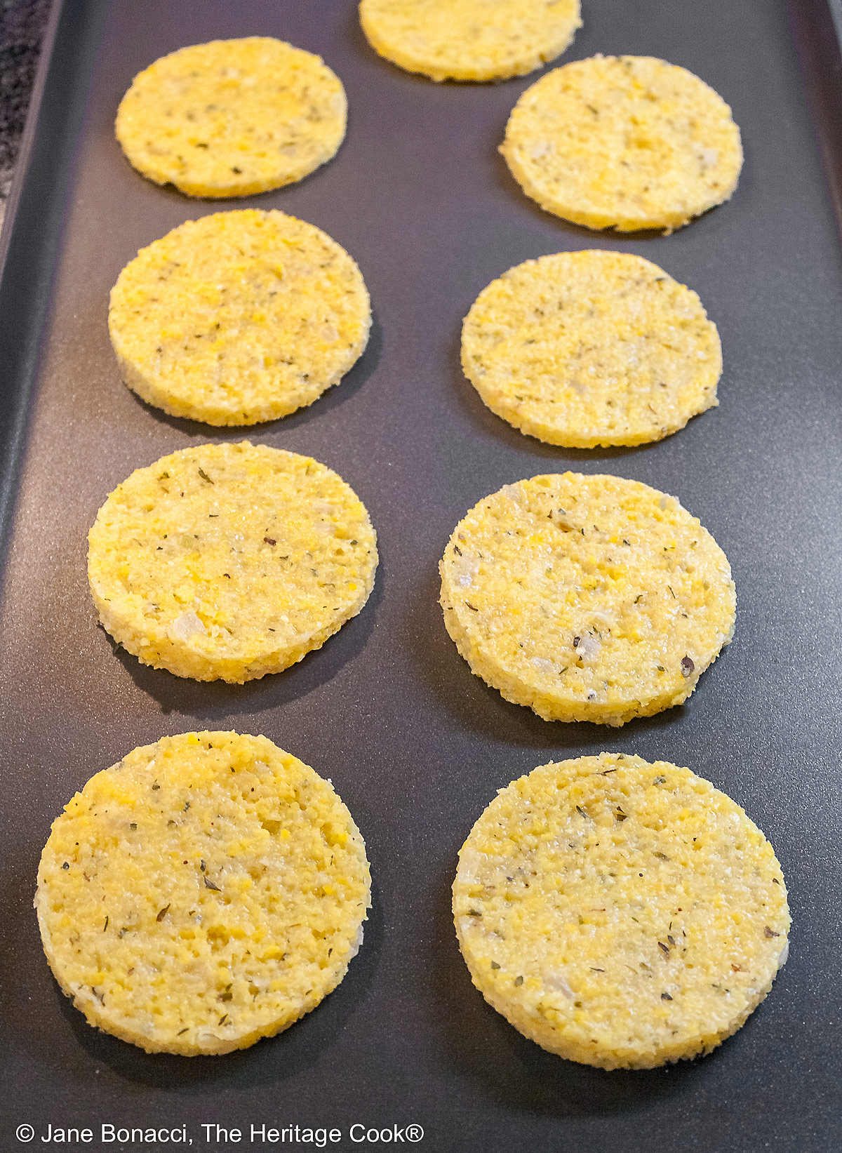 Griddle with two lines of polenta disks on it, ready to be crisped.
