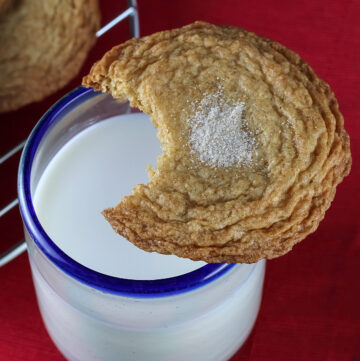 Single bite taken out of a cookie that is balanced on the edge of a glass of milk © 2024 Jane Bonacci, The Heritage Cook.