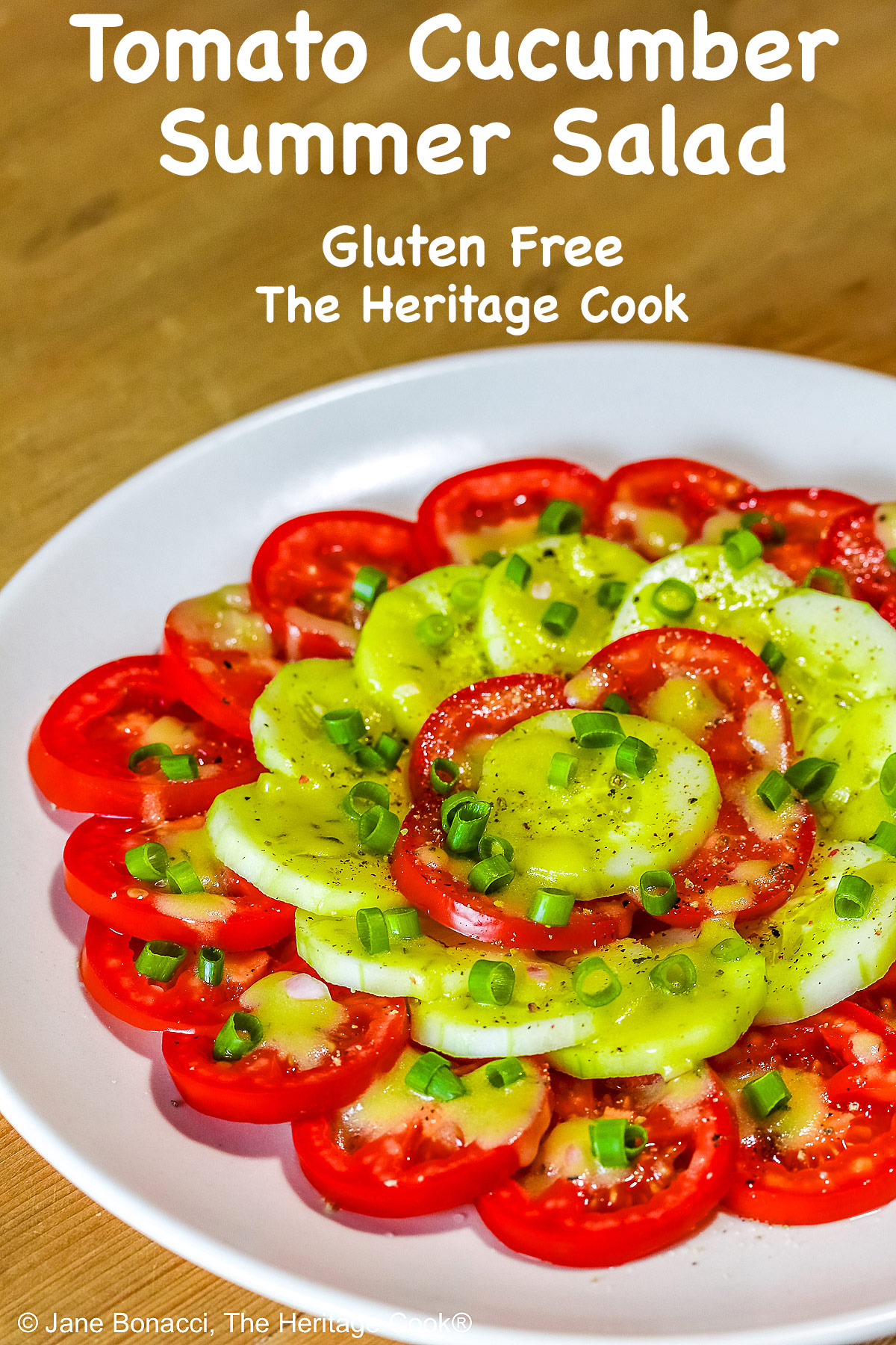 Concentric circles of tomatoes and cucumbers, each ring alternating between the two vegetables, drizzled with homemade vinaigrette and sprinkled with chopped green onions on a white plate © 2025 Jane Bonacci, The Heritage Cook. 