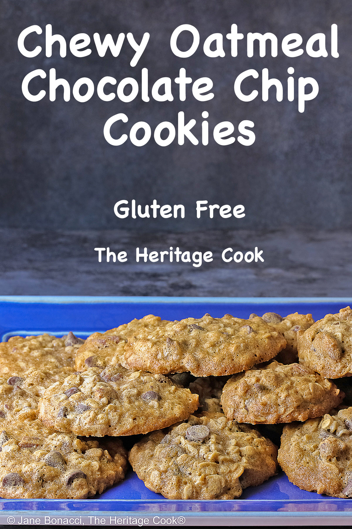 A large pile of amazing, delicious Chewy Oatmeal Chocolate Chip Cookies stacked on a rectangular blue platter sitting on a mottled gray background © 2026 Jane Bonacci, The Heritage Cook.