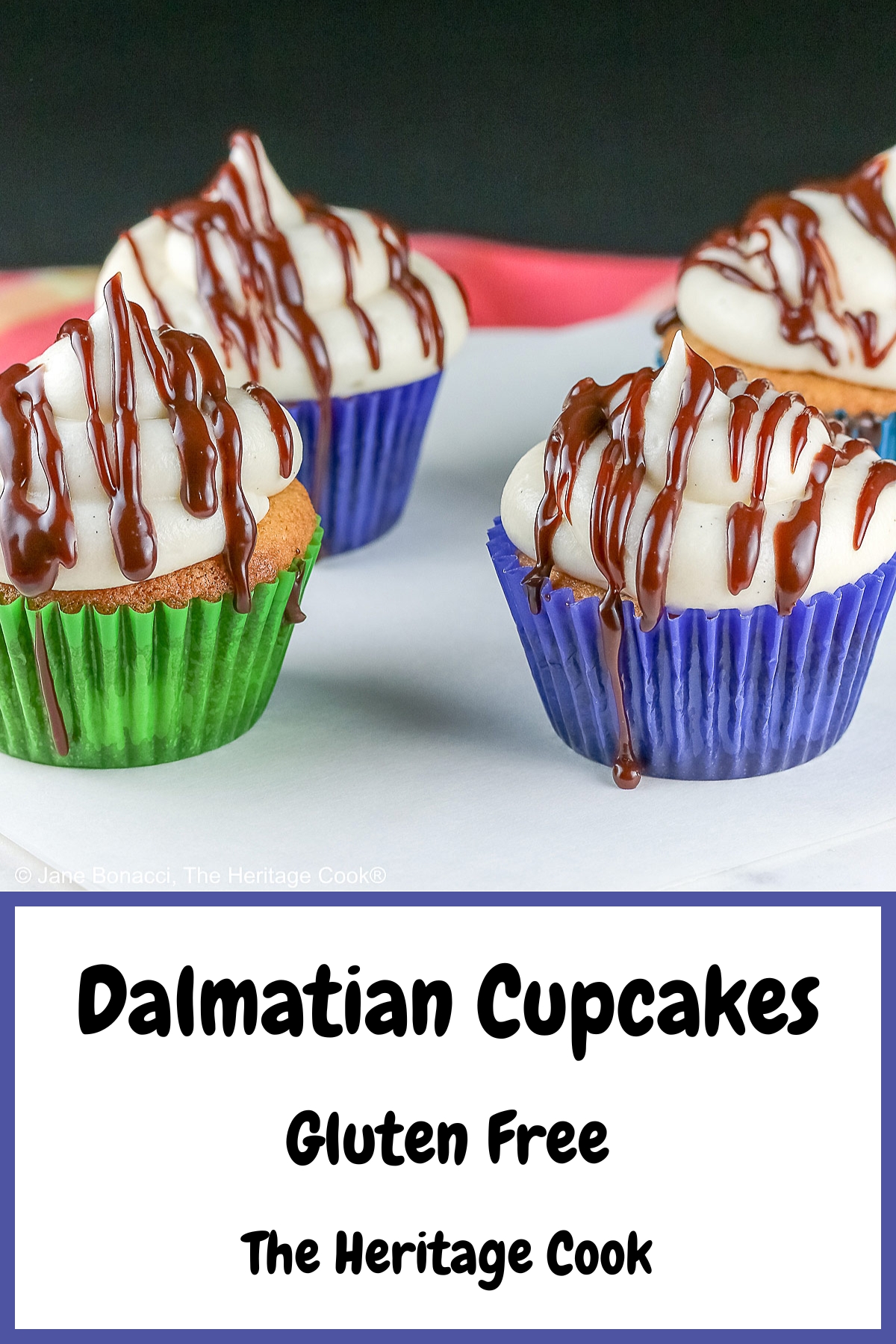 Dalmatian Cupcakes in a variety of bold colored liners topped with mounds of white frosting and drizzled with chocolate ganache, sitting on a white surface with a black background © 2025 Jane Bonacci, The Heritage Cook.