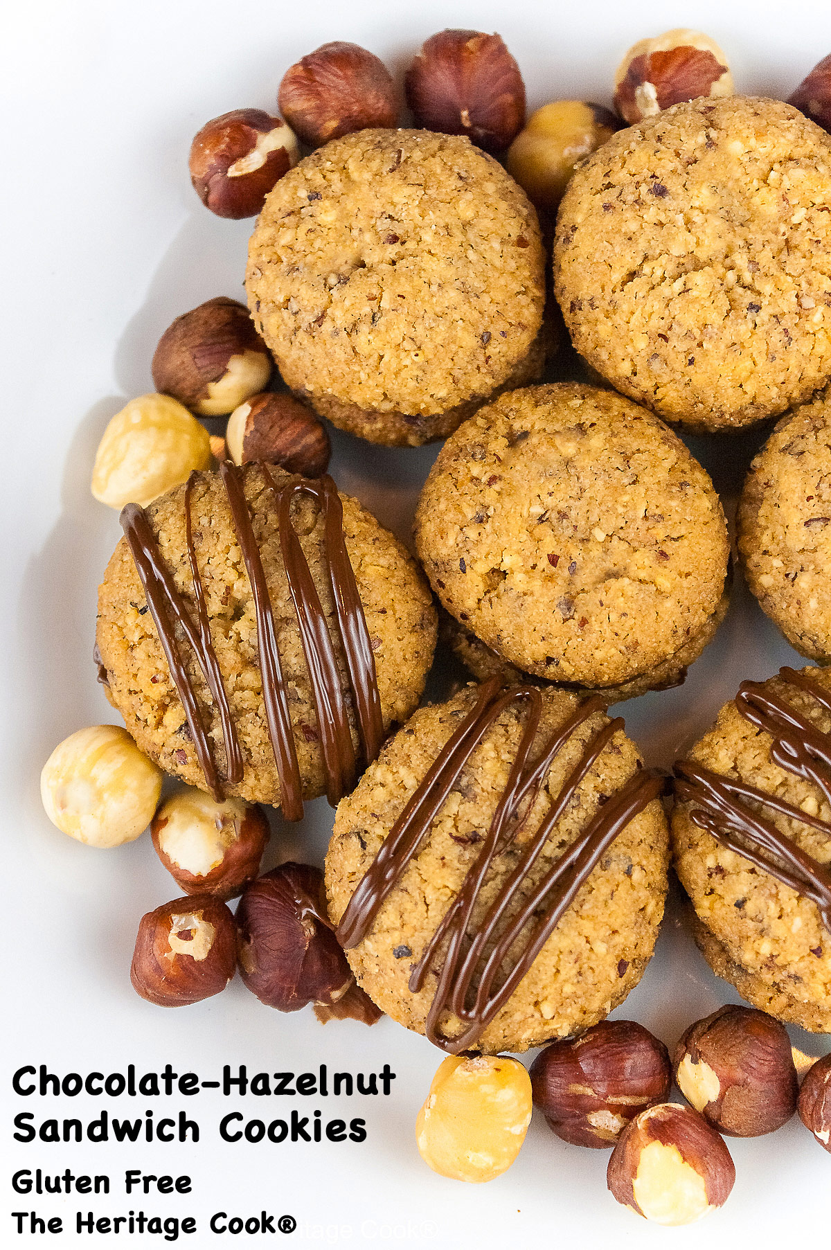 Chocolate Hazelnut Sandwich Cookies filled with chocolate ganache on a white plate sitting on a red, white, and green Italian towel, some drizzled with melted chocolate, with hazelnuts scattered around the cookies © 2026 Jane Bonacci, The Heritage Cook.
