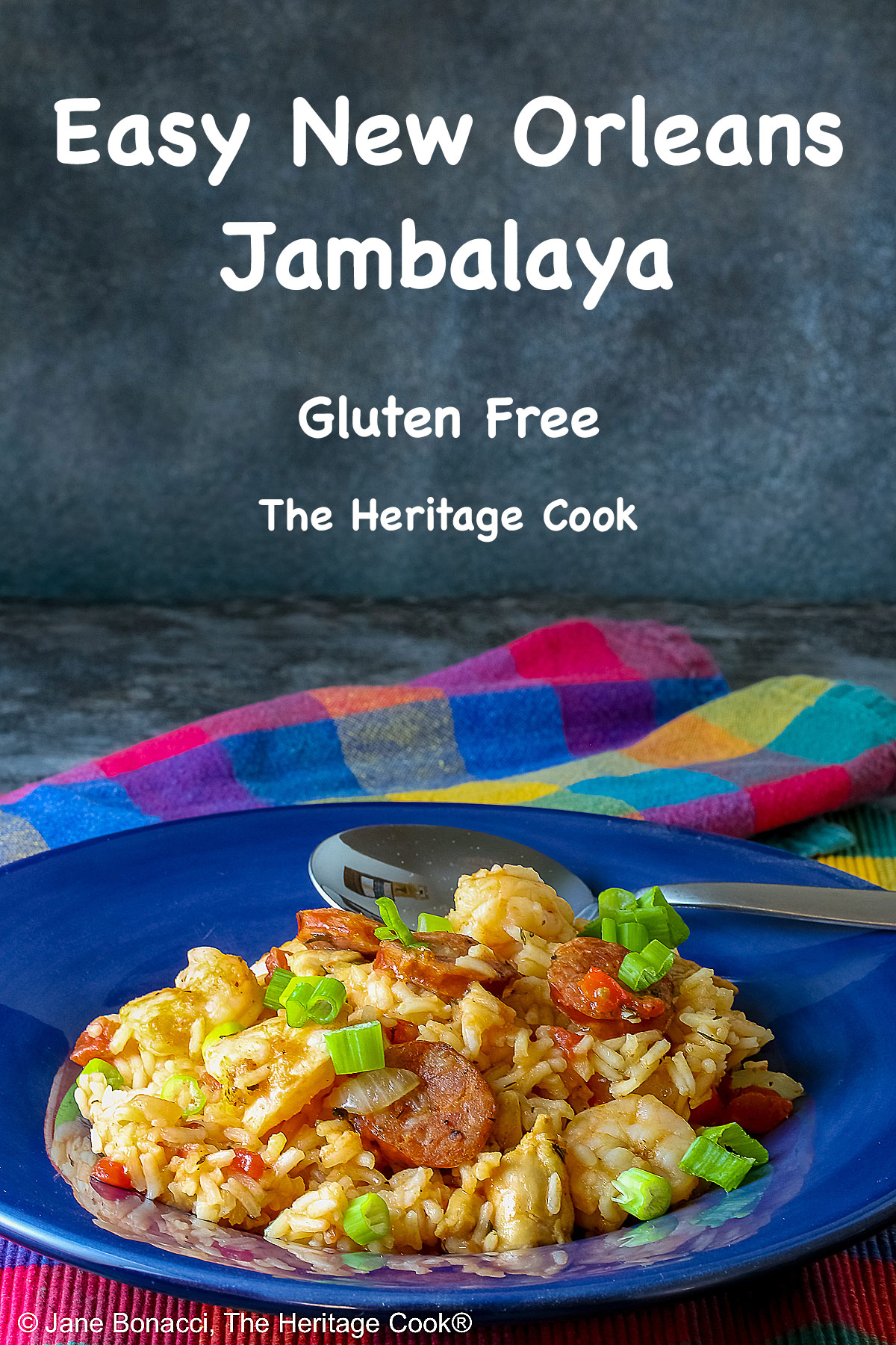 Mound of Easy New Orleans Jambalaya with chicken, shrimp, and sausages prominently placed and sprinkled with sliced green onions all in a dark blue bowl sitting on a brightly colored checked cloth © 2026 Jane Bonacci, The Heritage Cook.