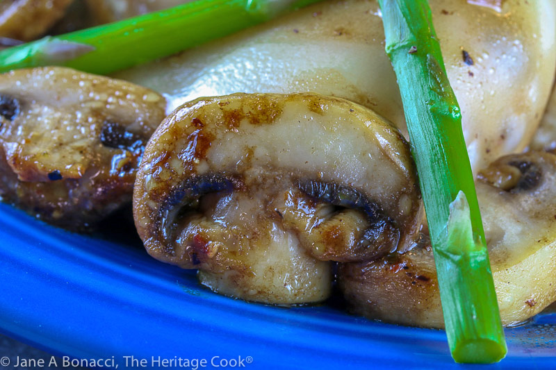 Close up of a mushroom; Cheesecake Factory's Chicken Madeira copycat recipe – chicken with melted cheese on top, crisscrossed asparagus spears on top and mushrooms scattered around in a rich, dark sauce © 2021 Jane Bonacci, The Heritage Cook
