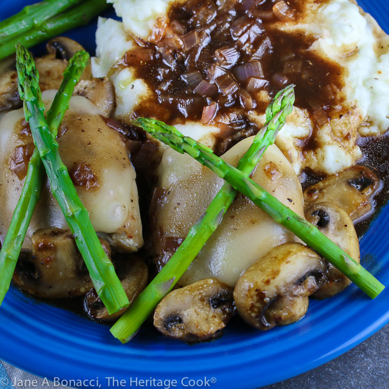 Cheesecake Factory's Chicken Madeira copycat recipe – chicken with melted cheese on top, crisscrossed asparagus spears on top and mushrooms scattered around in a rich, dark sauce © 2021 Jane Bonacci, The Heritage Cook