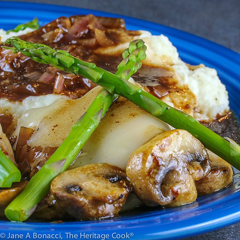 Cheesecake Factory's Chicken Madeira copycat recipe – chicken with melted cheese on top, crisscrossed asparagus spears on top and mushrooms scattered around in a rich, dark sauce © 2021 Jane Bonacci, The Heritage Cook