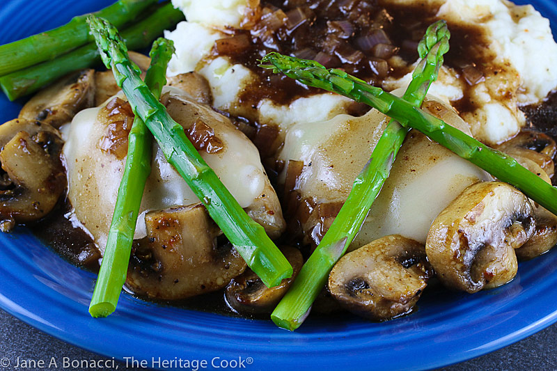 Cheesecake Factory's Chicken Madeira copycat recipe – chicken with melted cheese on top, crisscrossed asparagus spears on top and mushrooms scattered around in a rich, dark sauce © 2021 Jane Bonacci, The Heritage Cook