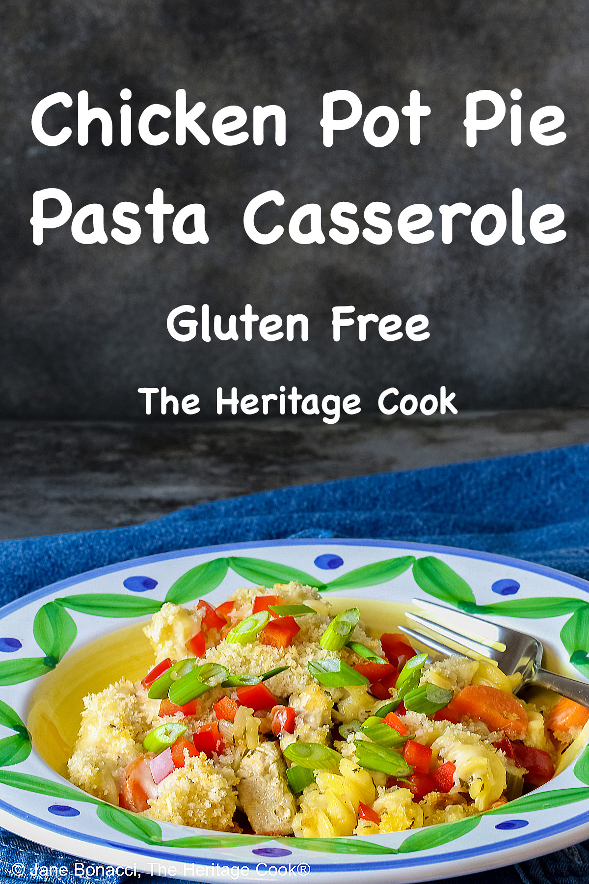 Bowl with a large rim decorated with green and blue designs filled with the Chicken Pot Pie Pasta Casserole that is topped with tiny squares of red bell pepper and sliced green onions on a blue denim cloth © 2026 Jane Bonacci, The Heritage Cook.