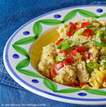Bowl with a large rim decorated with green and blue designs filled with the Chicken Pot Pie Pasta Casserole that is topped with tiny squares of red bell pepper and sliced green onions on a blue denim cloth © 2026 Jane Bonacci, The Heritage Cook.