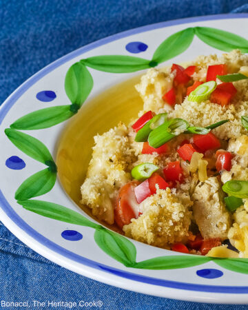 Bowl with a large rim decorated with green and blue designs filled with the Chicken Pot Pie Pasta Casserole that is topped with tiny squares of red bell pepper and sliced green onions on a blue denim cloth © 2026 Jane Bonacci, The Heritage Cook.
