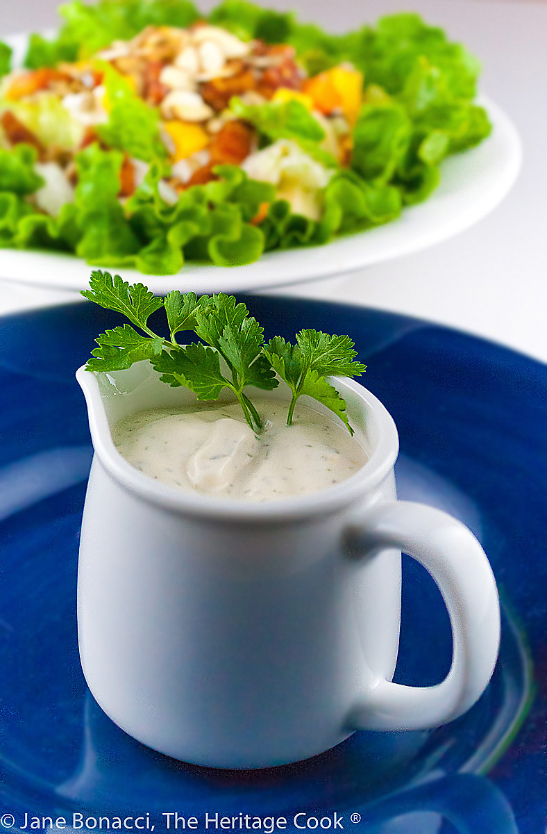 pitcher with dressing and a sprig of parsley in front of a large bowl of the chopped salad