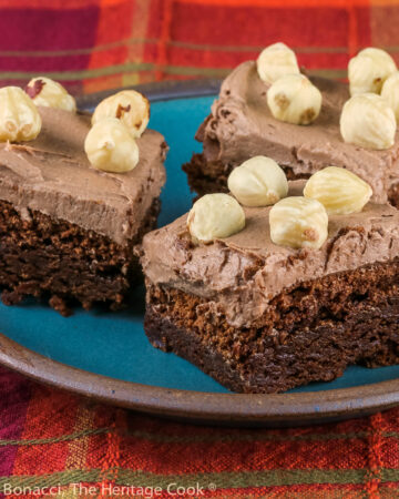 3 brownies on a blue plate, topped with Nutella frosting and studded with whole hazelnuts; Brownies with Nutella Frosting © 2022 Jane Bonacci, The Heritage Cook.