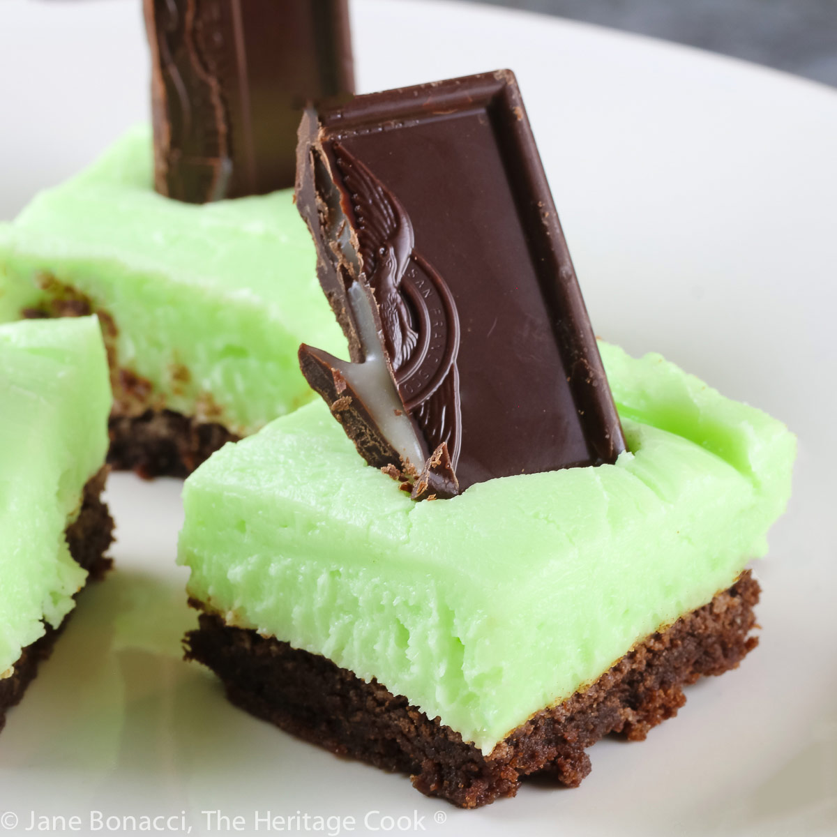 Brownies topped with pale green frosting with a chocolate-covered mint candy stuck in the top; Minty Chocolate Brownies © 2022 Jane Bonacci, The Heritage Cook.
