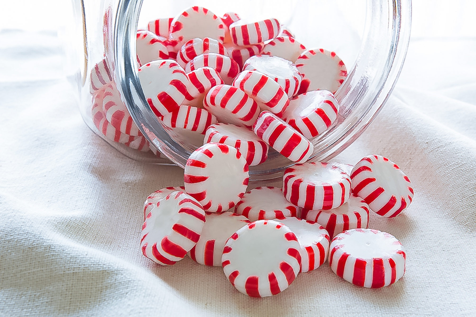 Jar of peppermint candies spilling out of a jar onto the table.