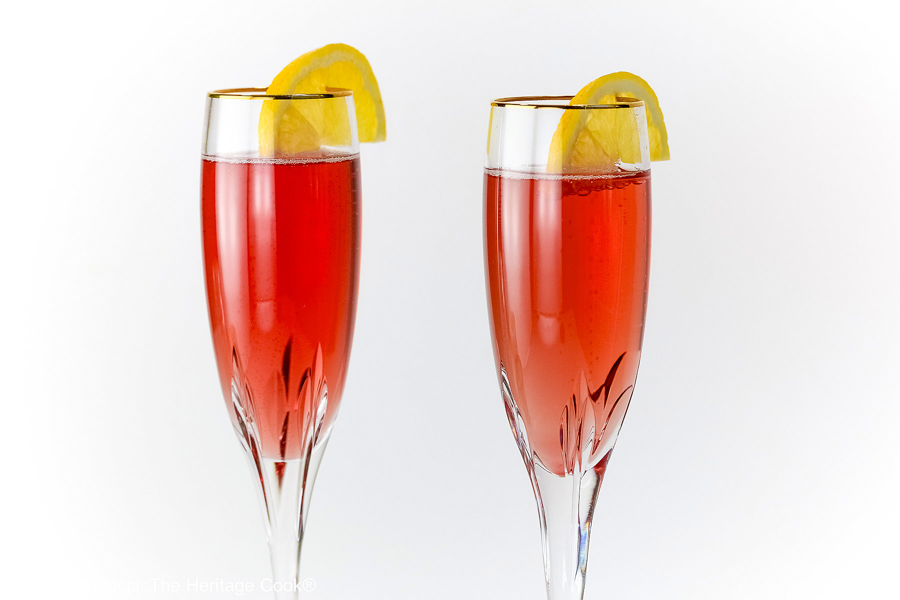 Kir Royale Champagne Cocktails are made with ruby red crème de cassis (black currant liqueur) combined with champagne to make these beautiful pink cocktails, served in crystal flutes on a white background © 2025 Jane Bonacci, The Heritage Cook.