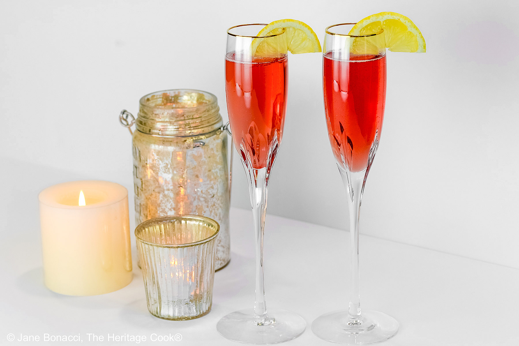 Kir Royale Champagne Cocktails are made with ruby red crème de cassis (black currant liqueur) combined with champagne to make these beautiful pink cocktails, served in crystal flutes on a white background © 2025 Jane Bonacci, The Heritage Cook.