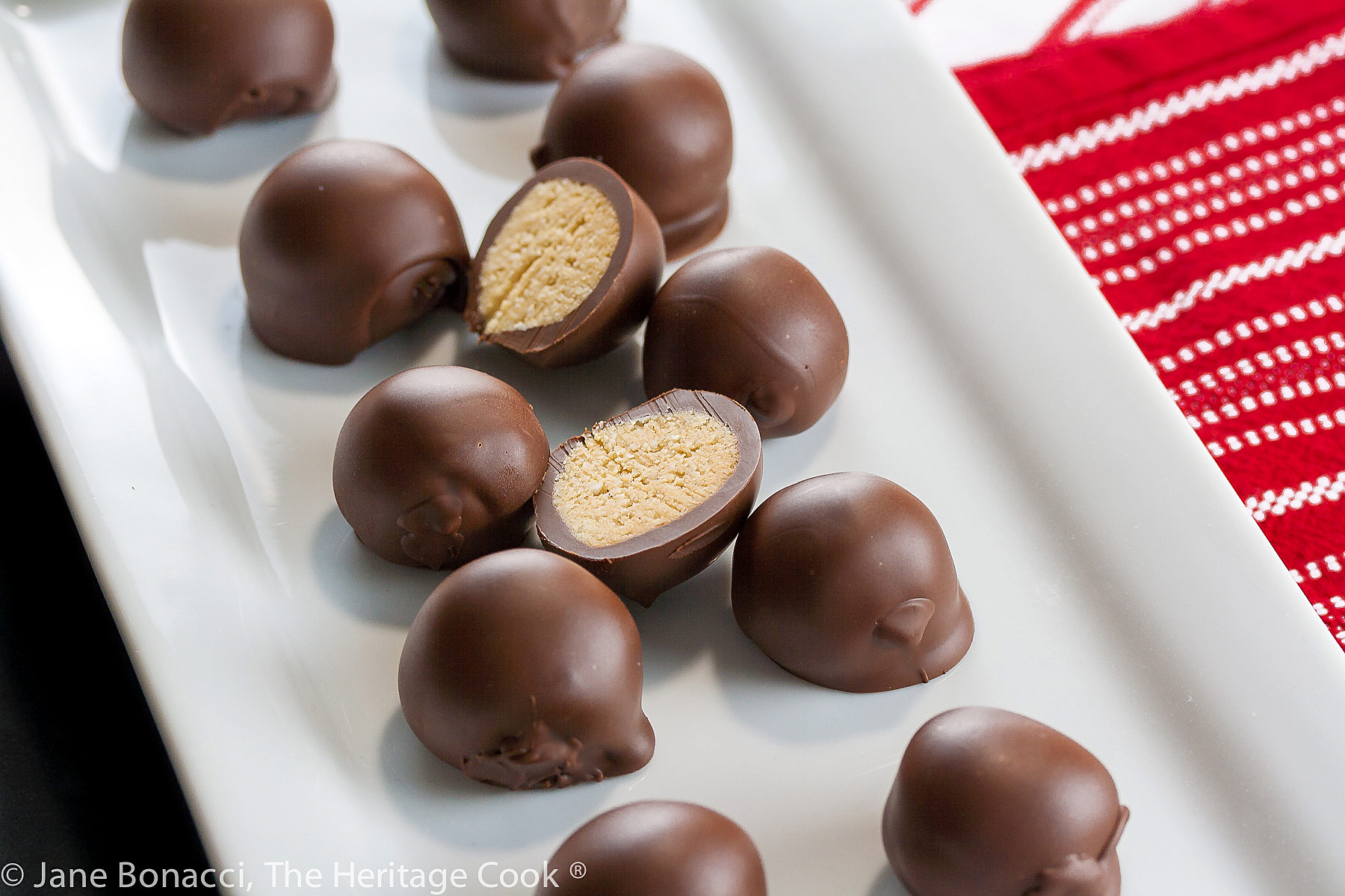 Chocolate covered round coconut and almond truffles on white plate or small platter, some cut in half to show centers; Almond Coconut Truffles © 2022 Jane Bonacci, The Heritage Cook. 