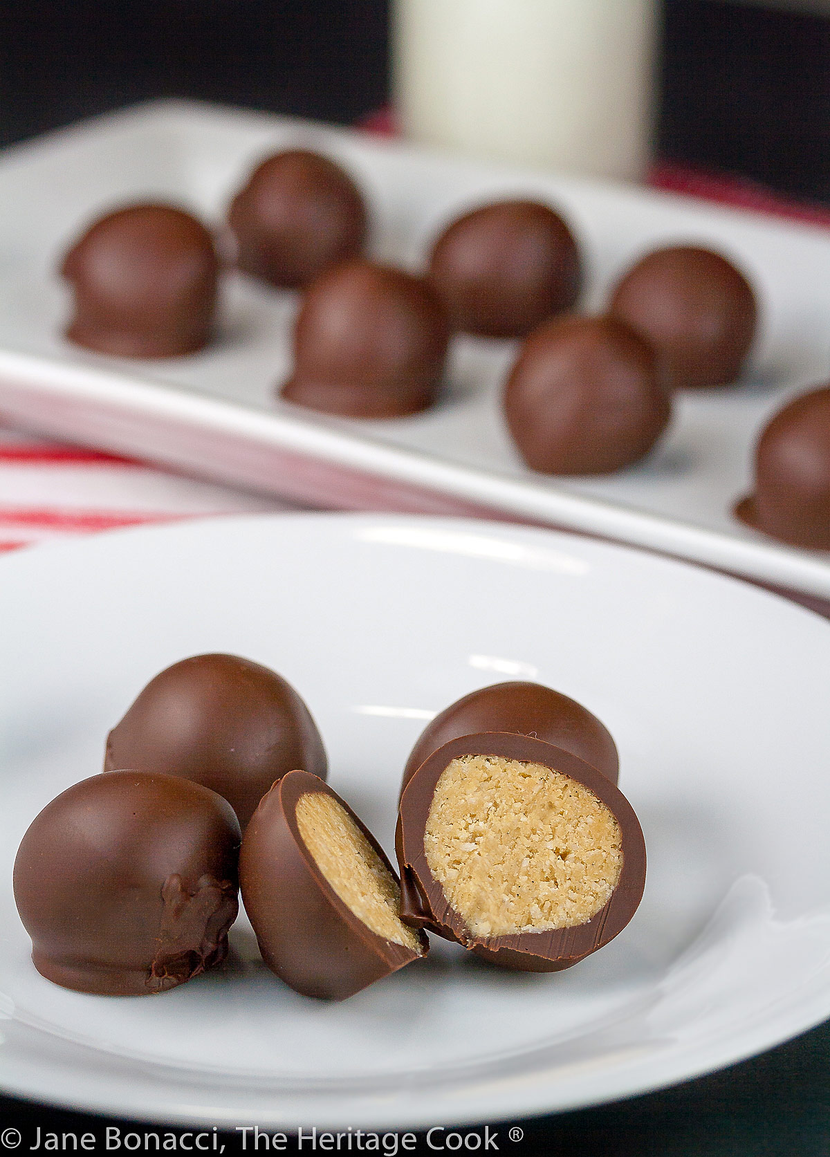 Chocolate covered round coconut and almond truffles on white plate or small platter, some cut in half to show centers; Almond Coconut Truffles © 2022 Jane Bonacci, The Heritage Cook. 