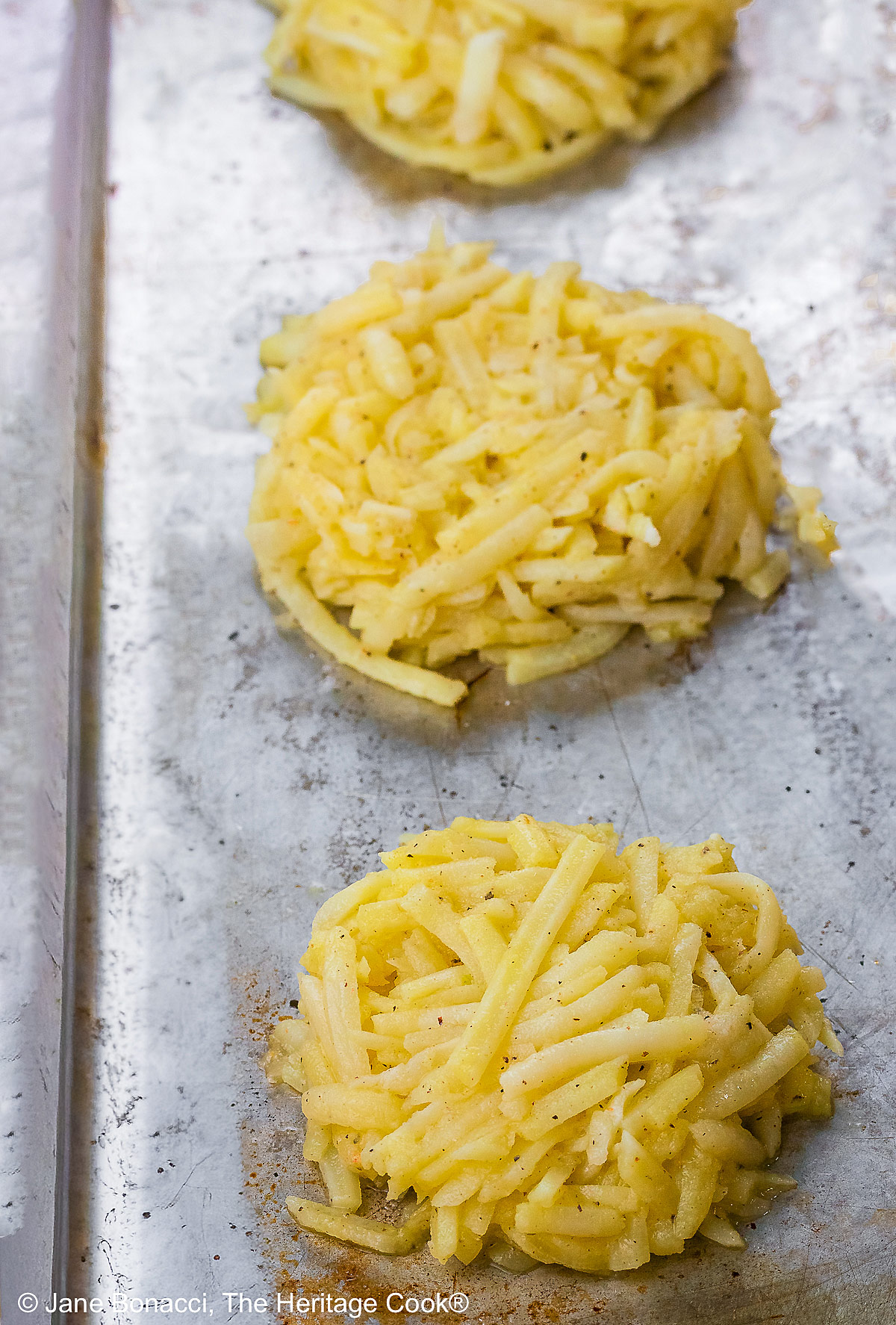 Two beautifully poached eggs laid on top of a slice of ham on a fried hash brown patty and topped with bright green hollandaise sauce, orange bell pepper cubes, and chives to mimic the colors of the Irish flag, on a white plate with two slices of lemon © 2026 Jane Bonacci, The Heritage Cook.