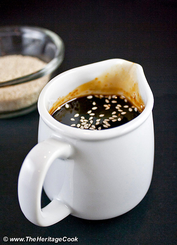 Small pitcher of teriyaki sauce sprinkled with white sesame seeds. 