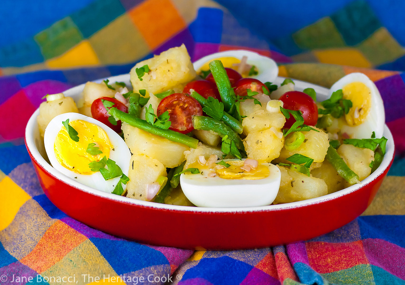 French Potato Salad with green beans in an au gratin dish with some cherry tomatoes and hard boiled eggs; Jane Bonacci, The Heritage Cook. 