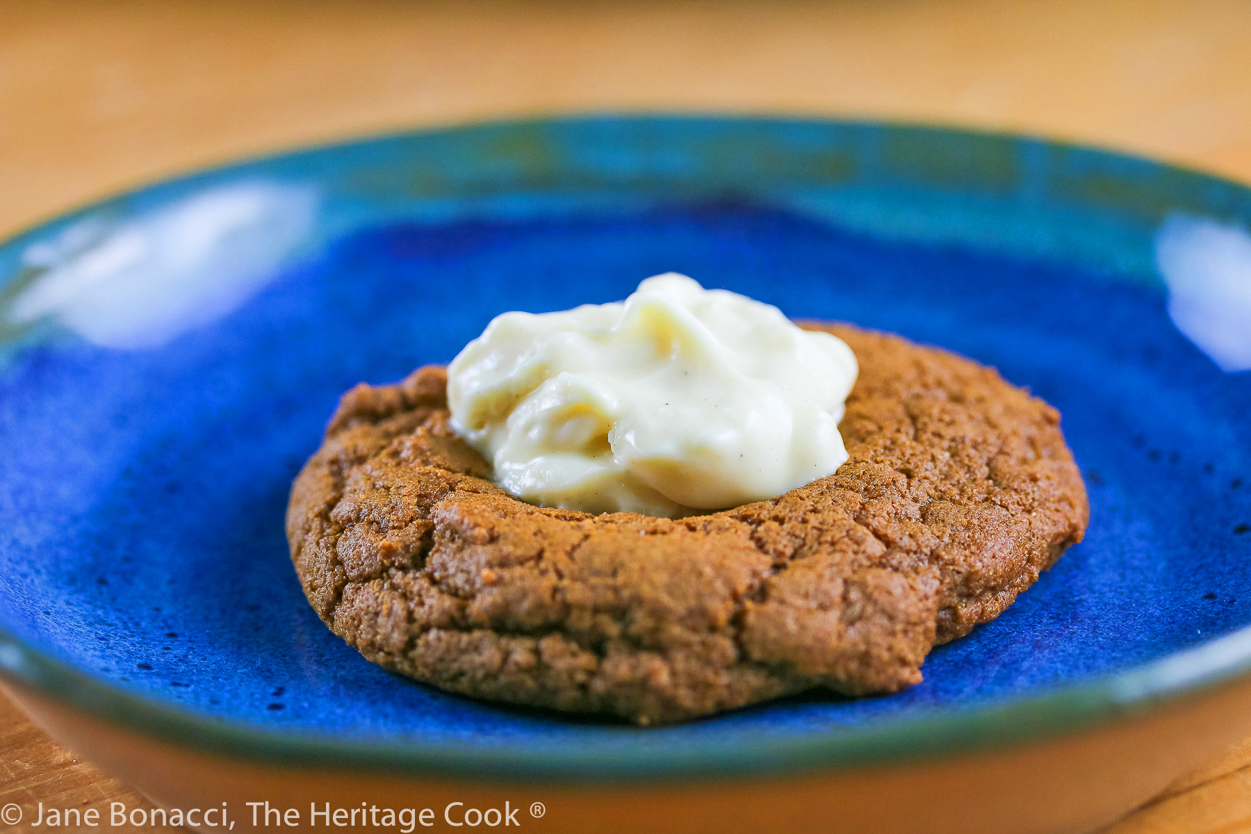 Brown, crackled cookies with melted white chocolate in the centers on a blue plate; Ginger White Chocolate Thumbprint Cookies © 2023 Jane Bonacci, The Heritage Cook. 