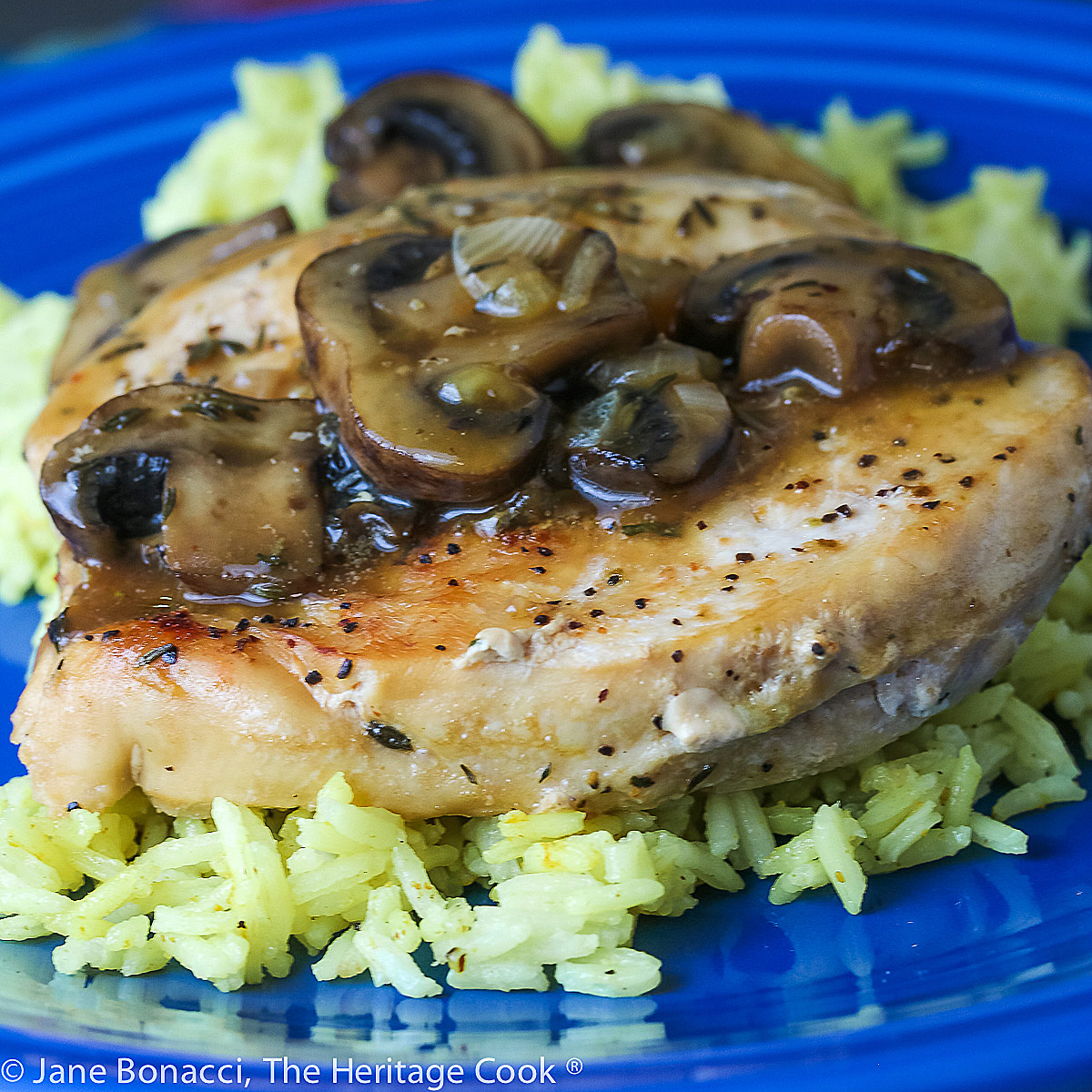 Butterflied chicken breast browned and covered with mushroom sauce, set on a bed of saffron rice on a deep blue plate; © 2023 Jane Bonacci, The Heritage Cook.