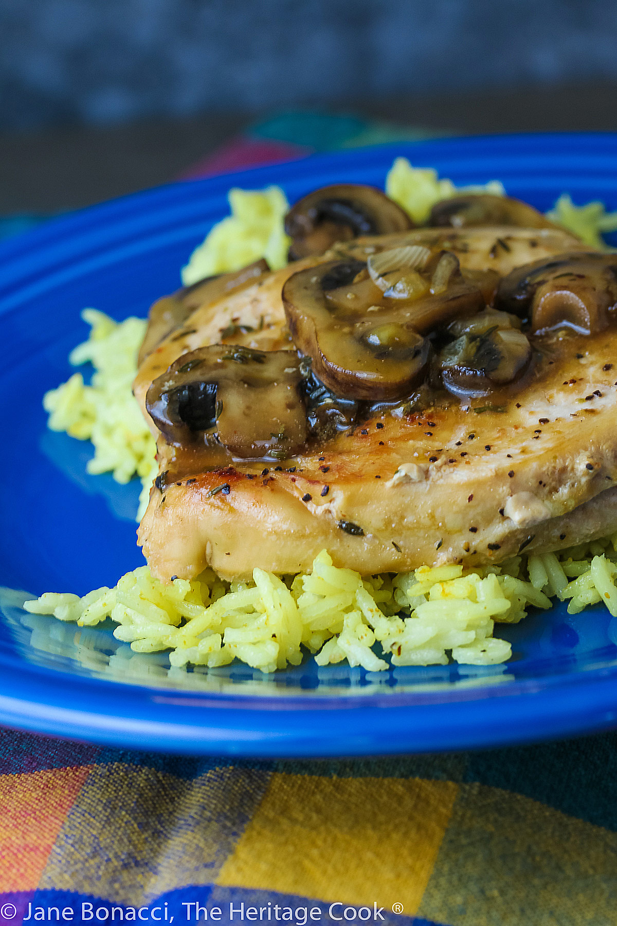 Butterflied chicken breast browned and covered with mushroom sauce, set on a bed of saffron rice on a deep blue plate; © 2023 Jane Bonacci, The Heritage Cook. 