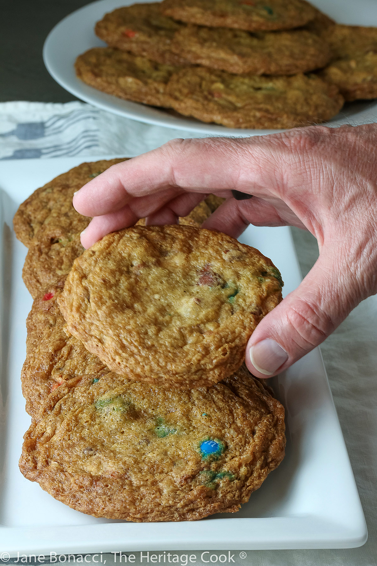Hand holding one cookie over the tray of cookies. 