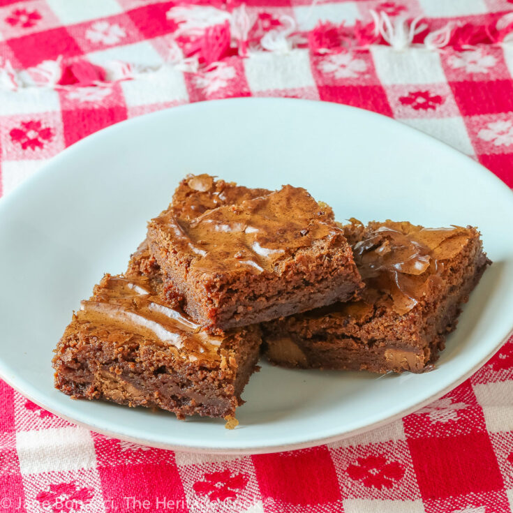 Stack of 4 brownies on white plate surrounded by red and white checked cloth, some close-ups; Triple Chocolate Brownies © 2023 Jane Bonacci, The Heritage Cook.