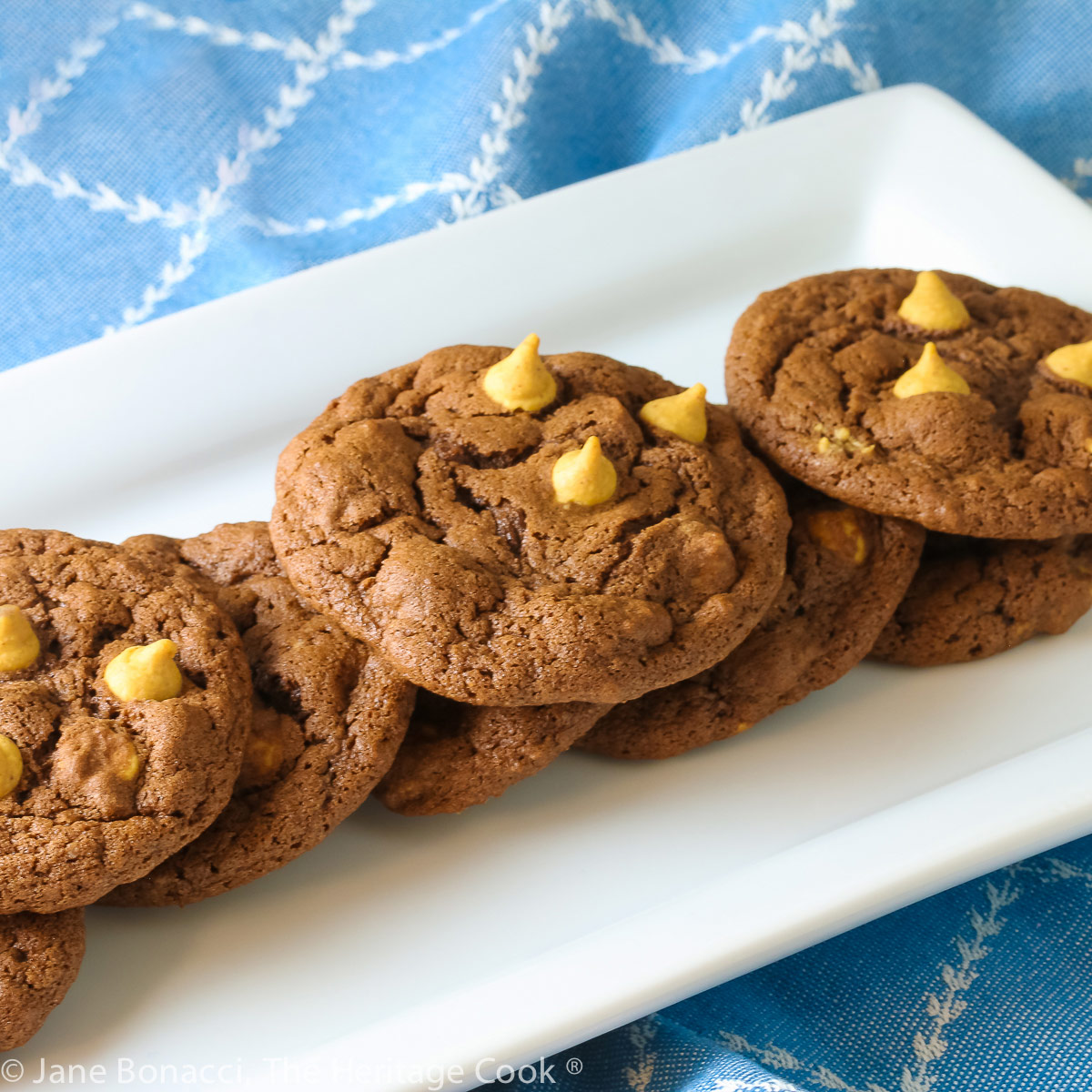 Chocolate cookies with lighter peanut butter chips on top on a white rectangular platter © 2023 Jane Bonacci, The Heritage Cook.