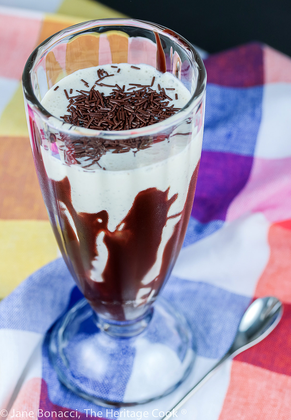 Vanilla ice cream blended with vanilla and milk, poured into a tall glass that has chocolate syrup drizzled around the inside in a swirling pattern © 2023 Jane Bonacci, The Heritage Cook. 