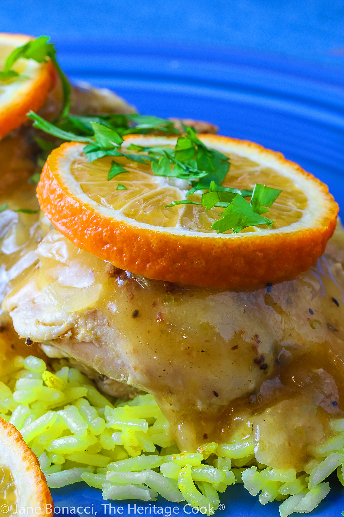 close up of a single chicken thigh on yellow rice topped with orange sauce, orange slice, and chopped cilantro. 