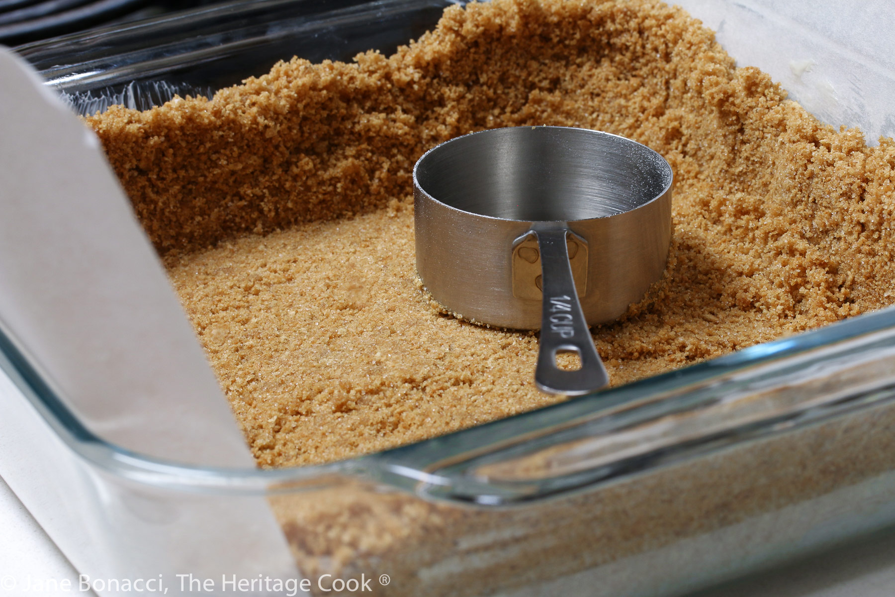 Using a flat-bottomed measuring cup to compact the graham cracker crust. 