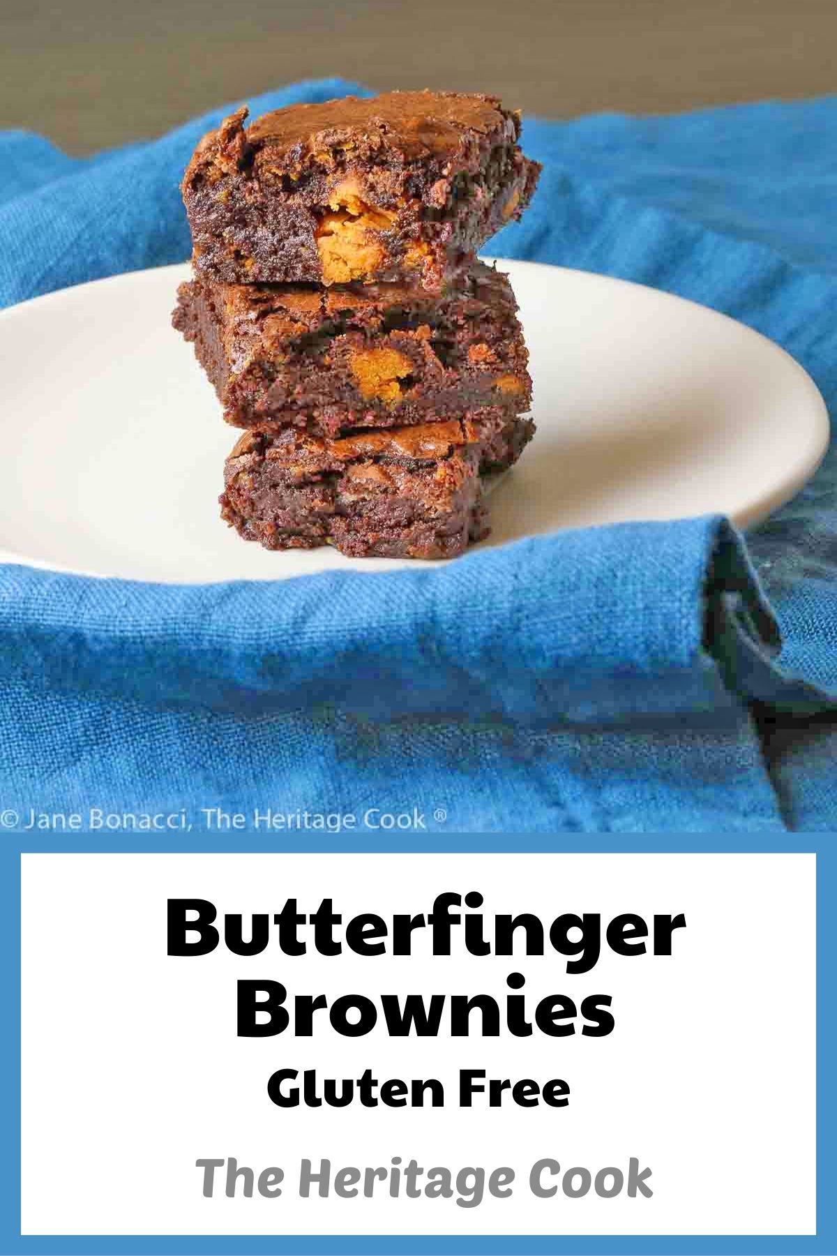 Butterfinger Brownies stacked on white plate with teal napkin background, one with a hand reaching for a brownie off the stack © 2023 Jane Bonacci, The Heritage Cook. 
