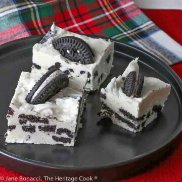 3 Squares of Cookies and Cream Fudge on a black plate on top of red and holiday plaid cloths © 2023 Jane Bonacci, The Heritage Cook.