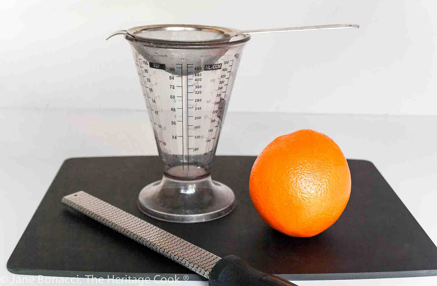 Set up for juicing the oranges with a zester, wire strainer in a measuring cup and an orange. . 