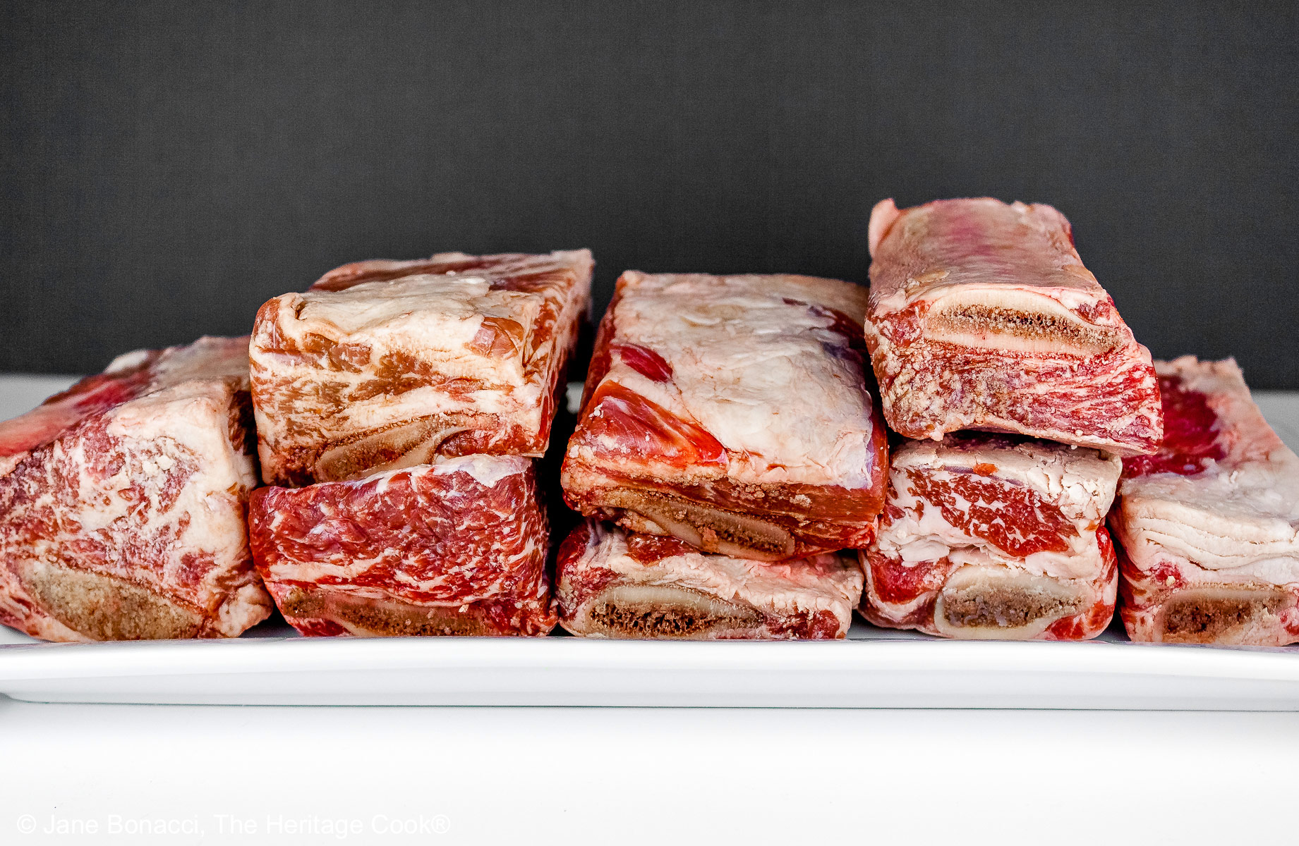 Garlic mashed potatoes lining a red bowl and topped with Red Wine Braised Short Ribs and carrots, in front of festive candles and Christmas decorations with holiday place mats © 2025 Jane Bonacci, The Heritage Cook.