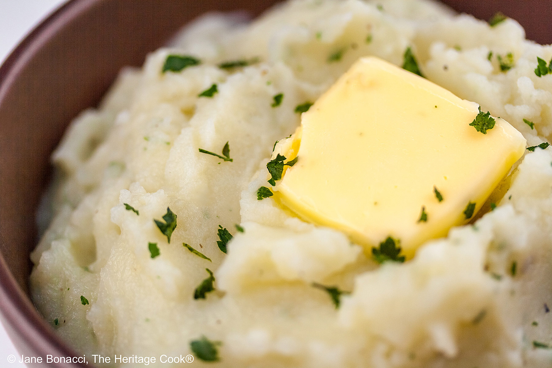 Bowl of piping hot garlic mashed potatoes with a melting pat of butter on top with a sprinkling of parsley.