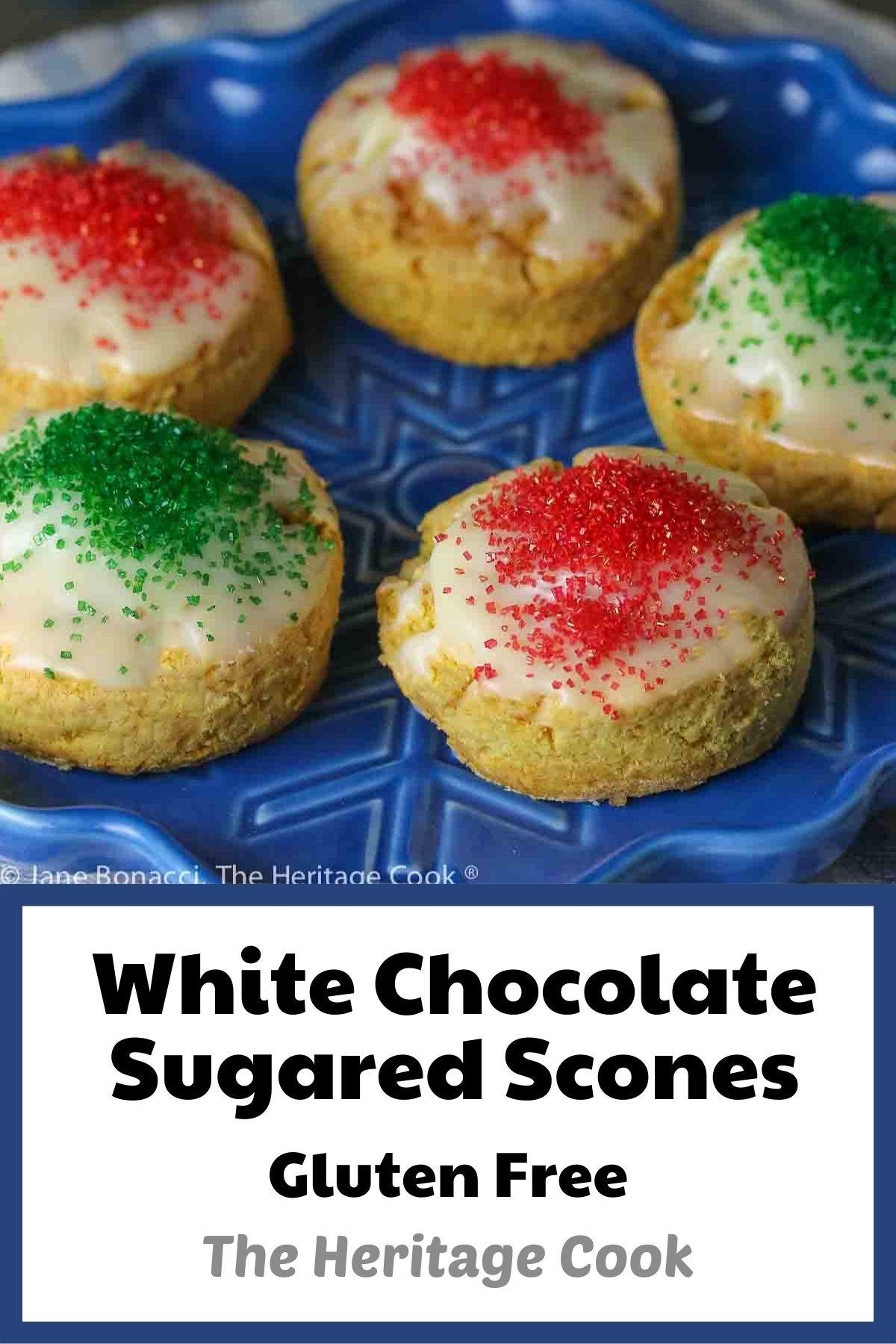 Five White Chocolate Sugared Scones with white chocolate glaze and sprinkled with red and green sugars, served on a blue star-shaped plate on top of a blue and white striped cloth, in front of festive hand-carved snowmen figures © 2023 Jane Bonacci, The Heritage Cook. 