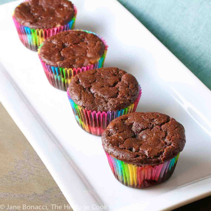 Chocolate Cheesecake Muffins baked in rainbow colored paper liners, lined up on a white rectangular platter © 2024 Jane Bonacci, The Heritage Cook.