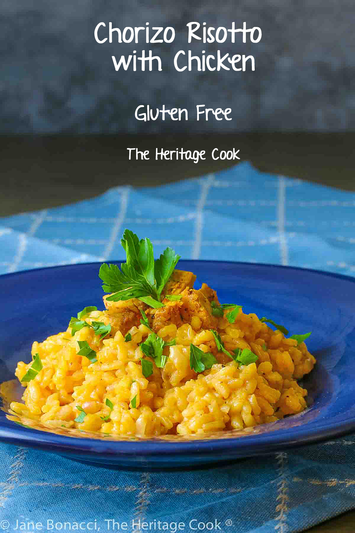 Golden rice piled in a dark blue bowl, topped with cubes of chicken and minced parsley, some with a spoon in the bowl © 2024 Jane Bonacci, The Heritage Cook. 