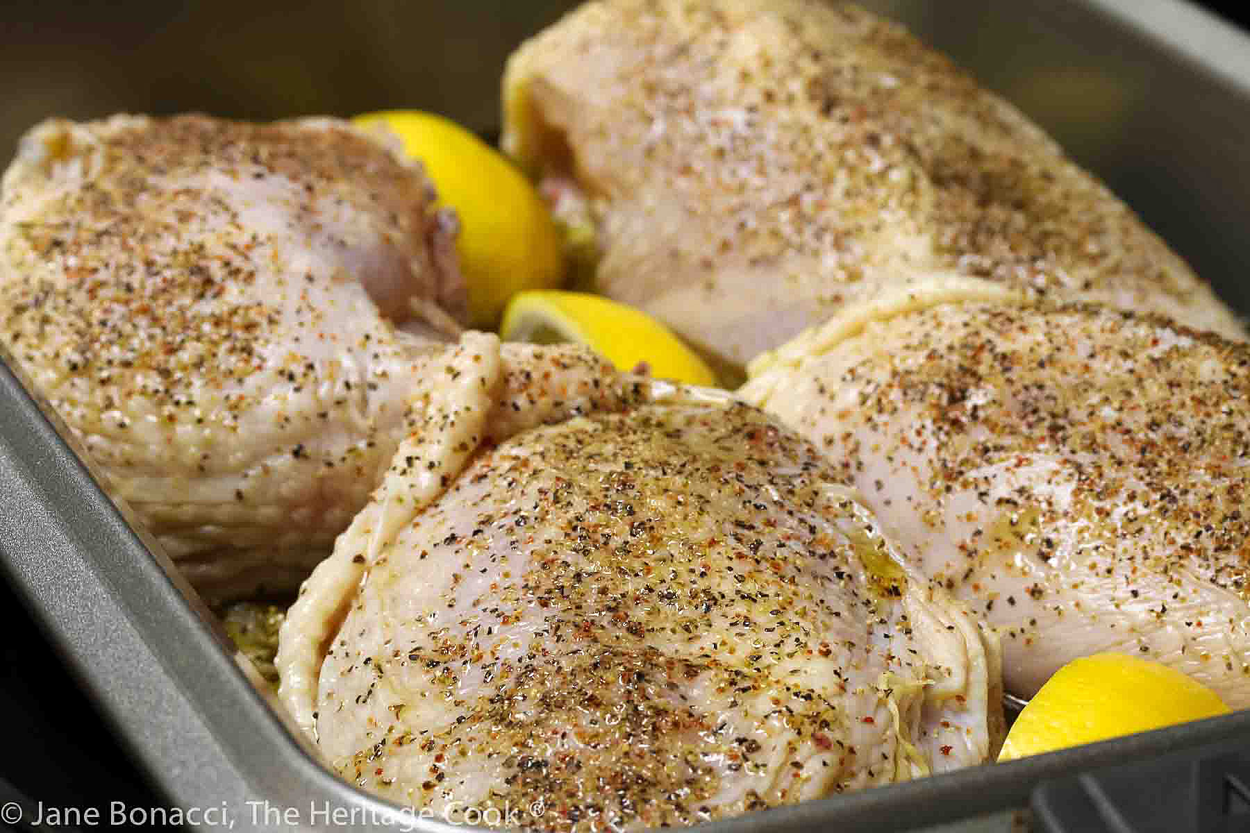 Chicken breasts seasoned and ready for the oven with lemon wedges tucked between them. 