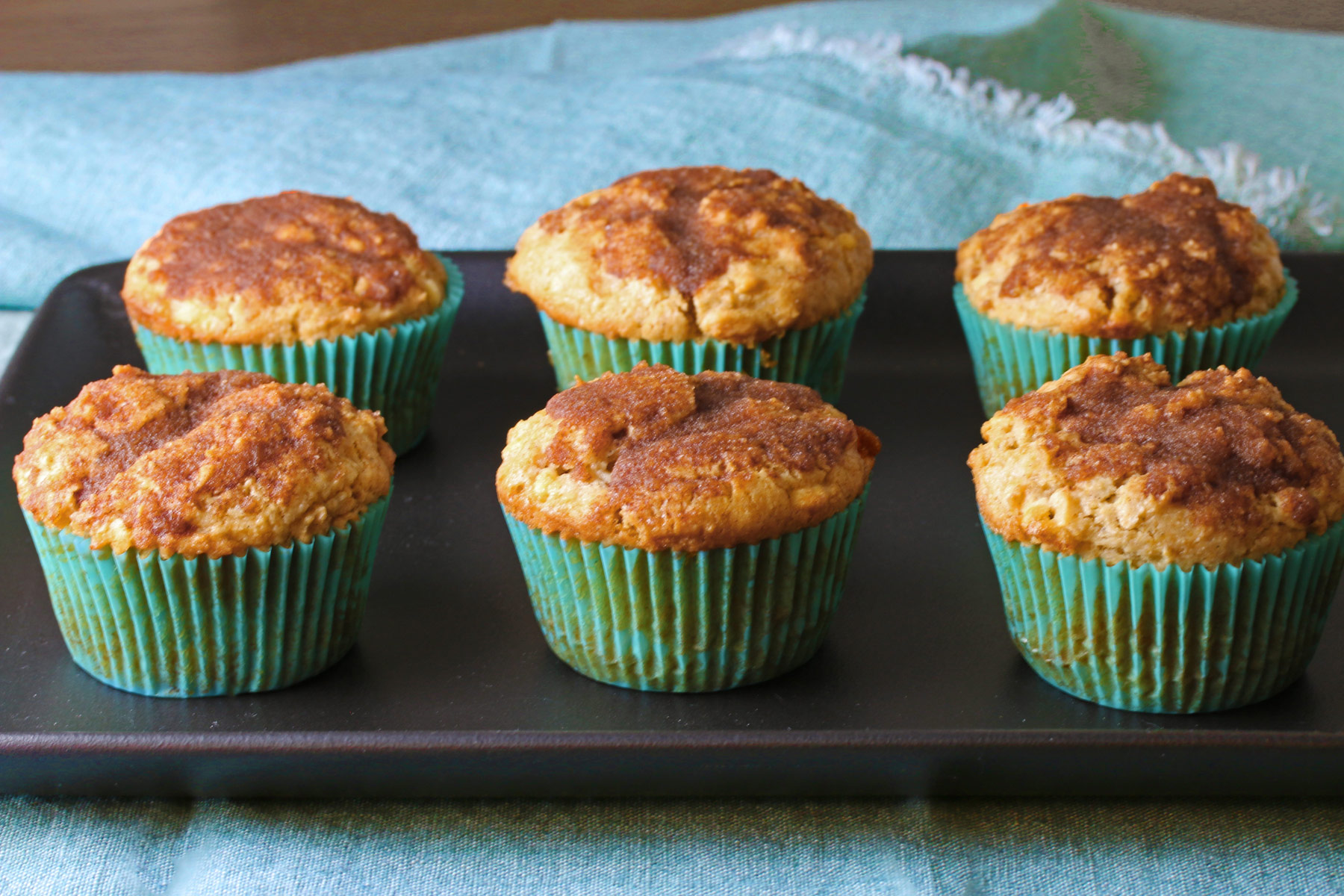 Snickerdoodle Muffins with White Chocolate lined up on a black tray with an aqua colored cloth around it © 2024 Jane Bonacci, The Heritage Cook. 